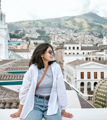 a young woman sits on a ledge overlooking Quito, Ecuador, insured with travel insurance for South America 