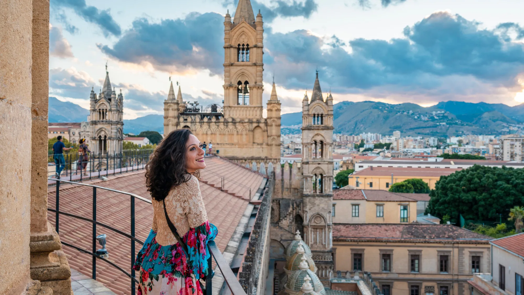 a middle-aged woman overlooks Sicily and Palermo's Cathedral on vacation after asking, "Is travel insurance worth it?"