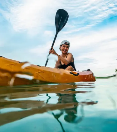 a woman with adventure travel insurance paddles her kayak through a crystal-clear lagoon