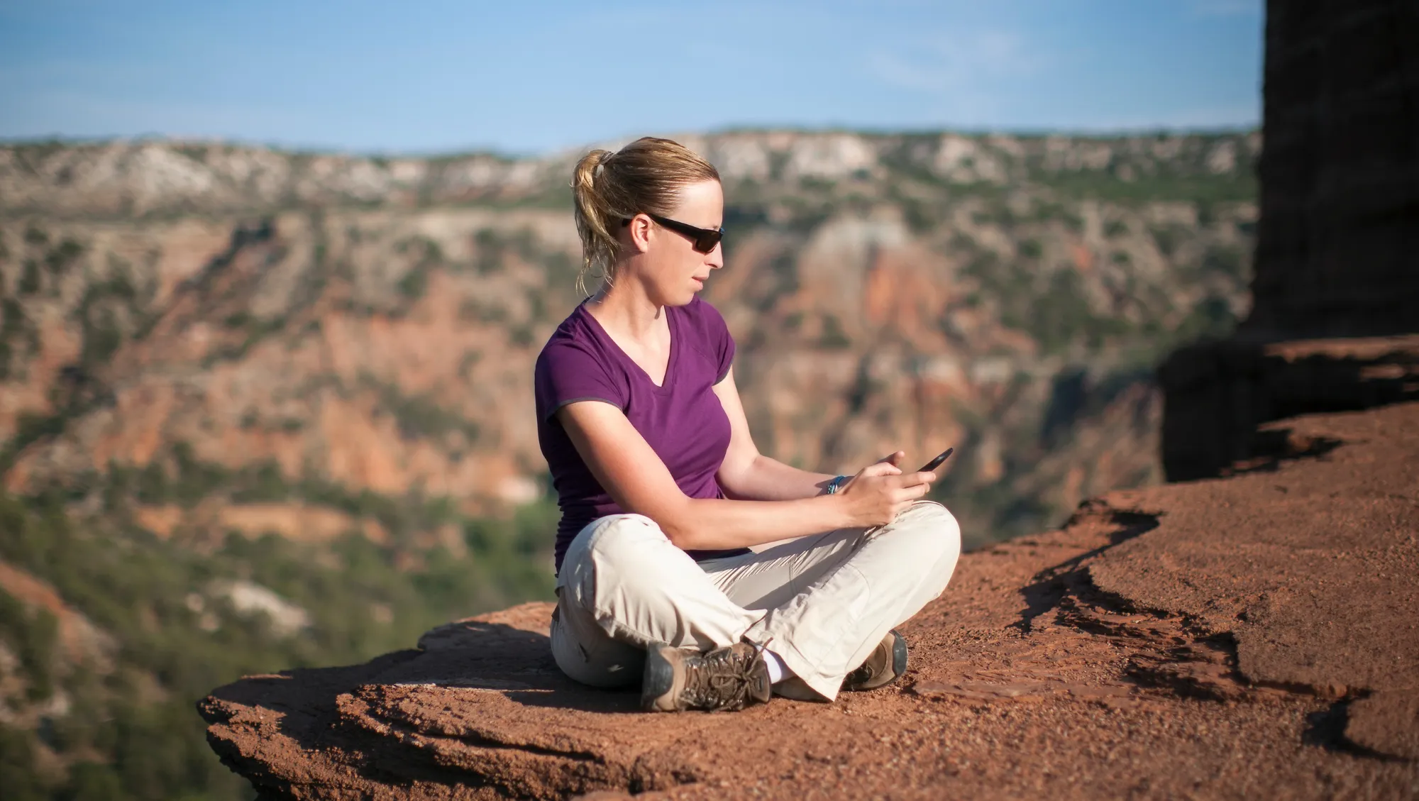 a woman sits and looks at the travel app on her phone in Palo Duro Canyon State Park 