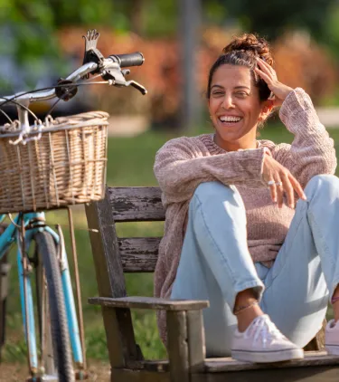 a young woman with travel insurance for Israel relaxes on a park bench next to a blue bicycle 
