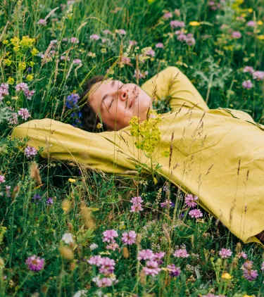 a woman with travel insurance for nature trips smiles as she rests in a wildflower field on vacation
