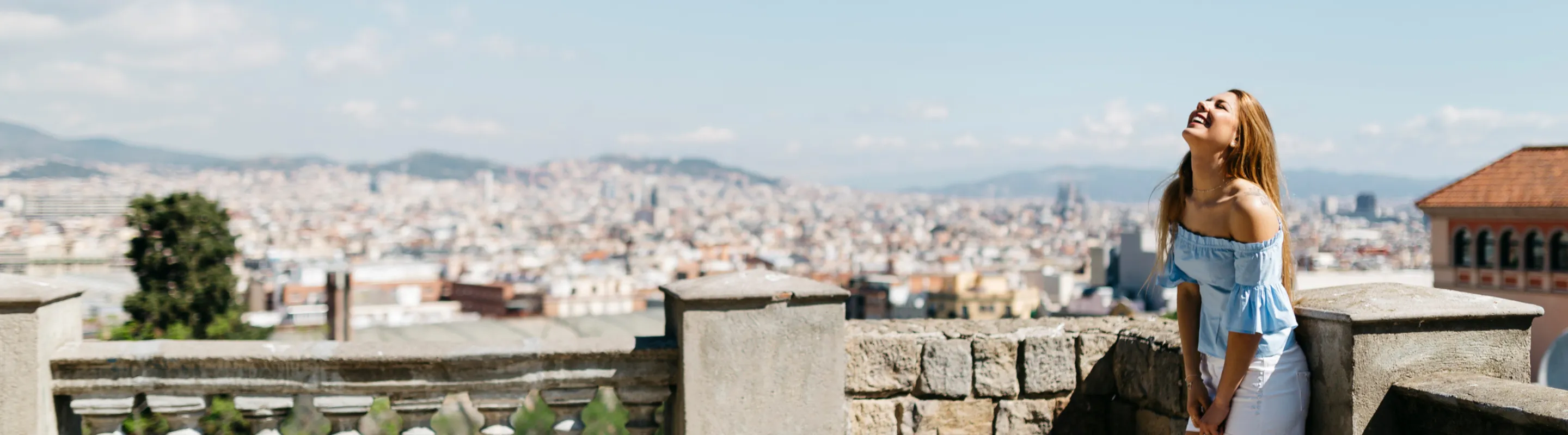 a woman with travel insurance for Spain, laughing on a rooftop terrace overlooking a city