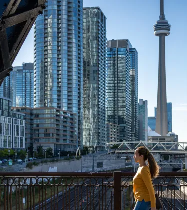 a woman in a yellow shirt walks through downtown Toronto, insured with travel insurance for Canada 