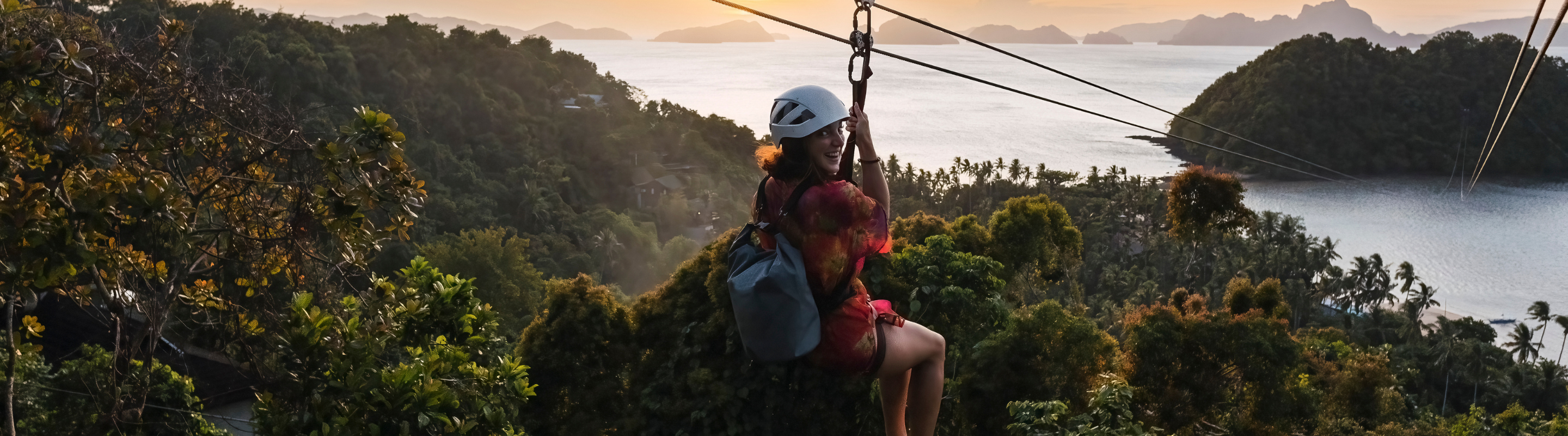 a woman with travel insurance for the Philippines rides a zipline above a tropical forest with coastal islands