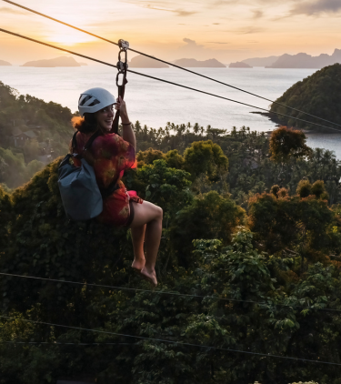 a woman with travel insurance for the Philippines rides a zipline above a tropical forest with coastal islands