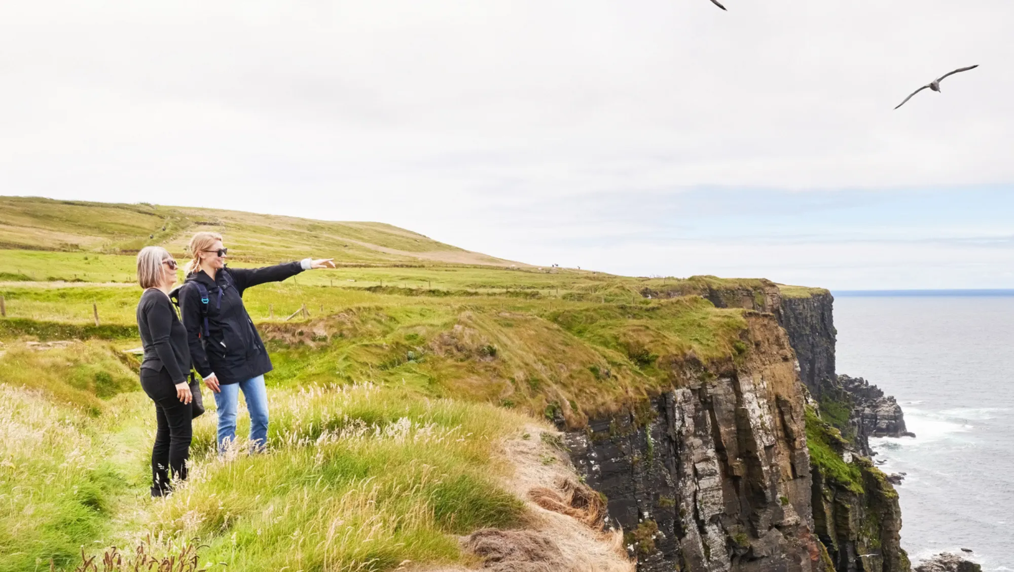 two women enjoy views on a cliff in Ireland on vacation after asking, "Is travel insurance worth it?"
