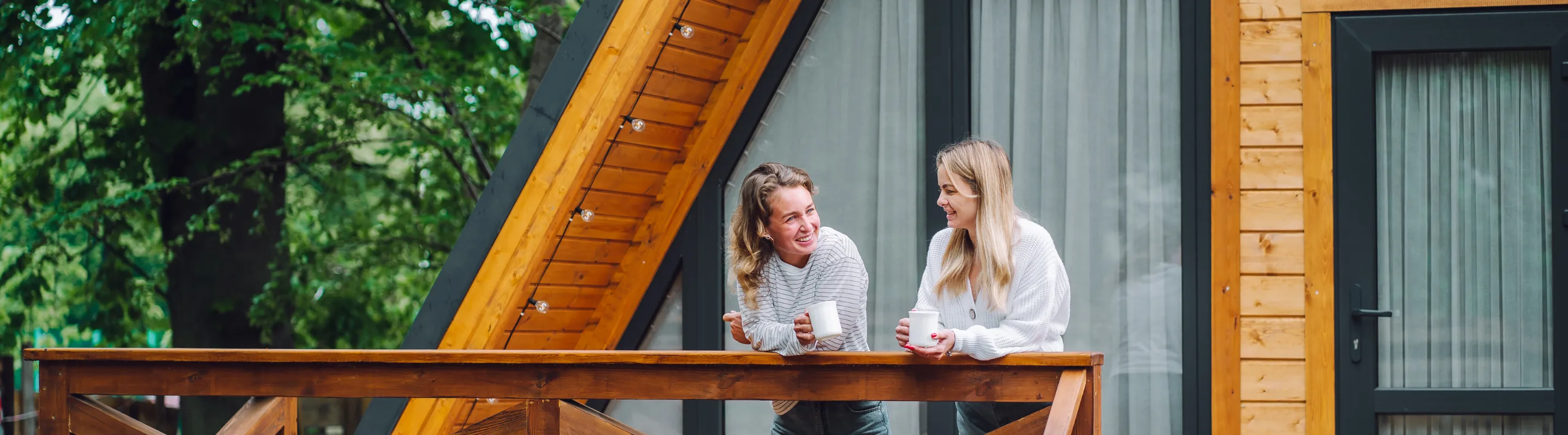 Two young women with vacation rental travel insurance having coffee on the front porch of a cabin