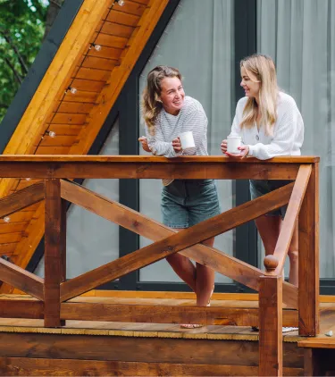Two young women with vacation rental travel insurance having coffee on the front porch of a cabin