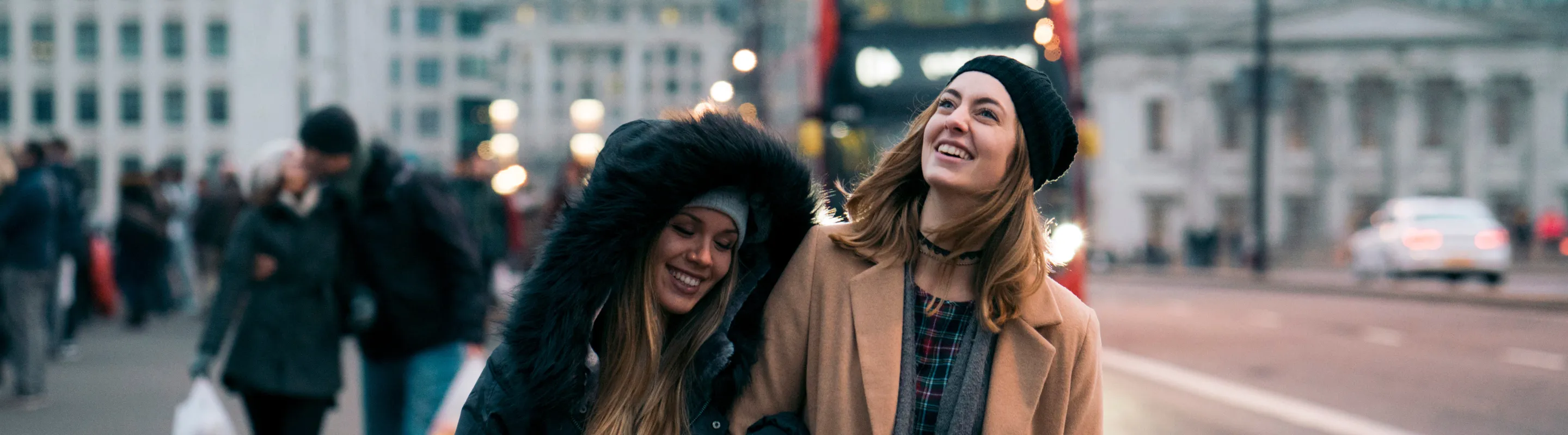 two women with travel insurance for the UK walk in central London with a red double-decker bus in the background