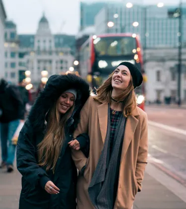 two women with travel insurance for the UK walk in central London with a red double-decker bus in the background