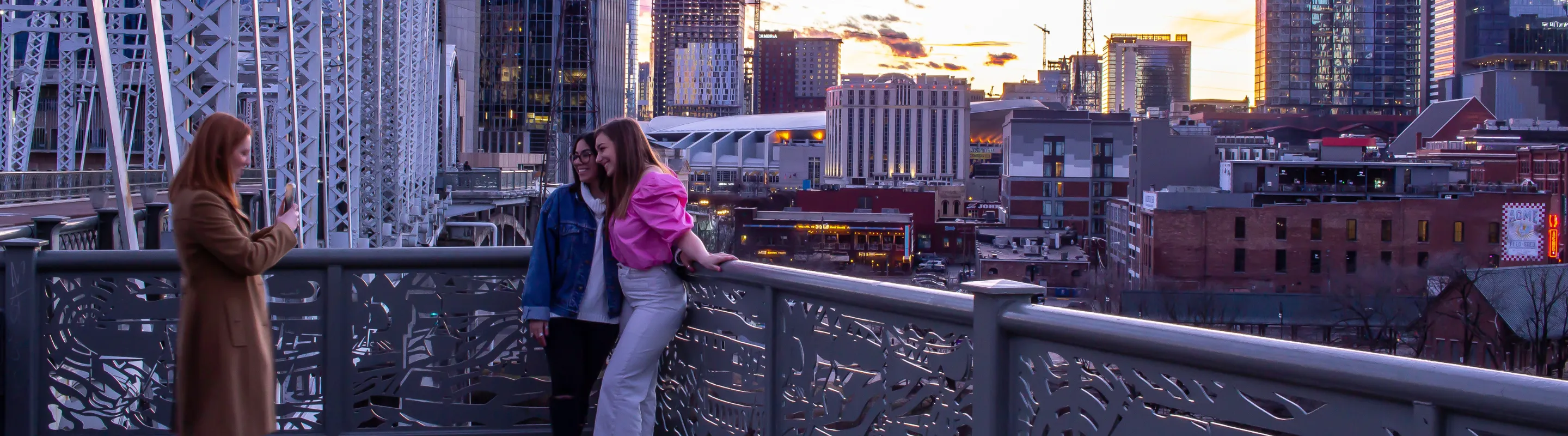 two women pose for a picture on a bridge in Nashville at sunset, insured with travel insurance for Tennessee 