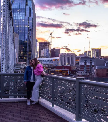 two women pose for a picture on a bridge in Nashville at sunset, insured with travel insurance for Tennessee 