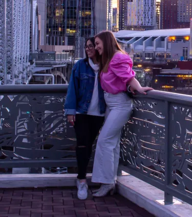 two women pose for a picture on a bridge in Nashville at sunset, insured with travel insurance for Tennessee 
