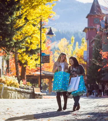 two women stand in Whistler Village with shopping bags in Autumn, insured with travel insurance for Canada