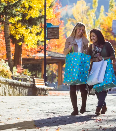 two women stand in Whistler Village with shopping bags in Autumn, insured with travel insurance for Canada