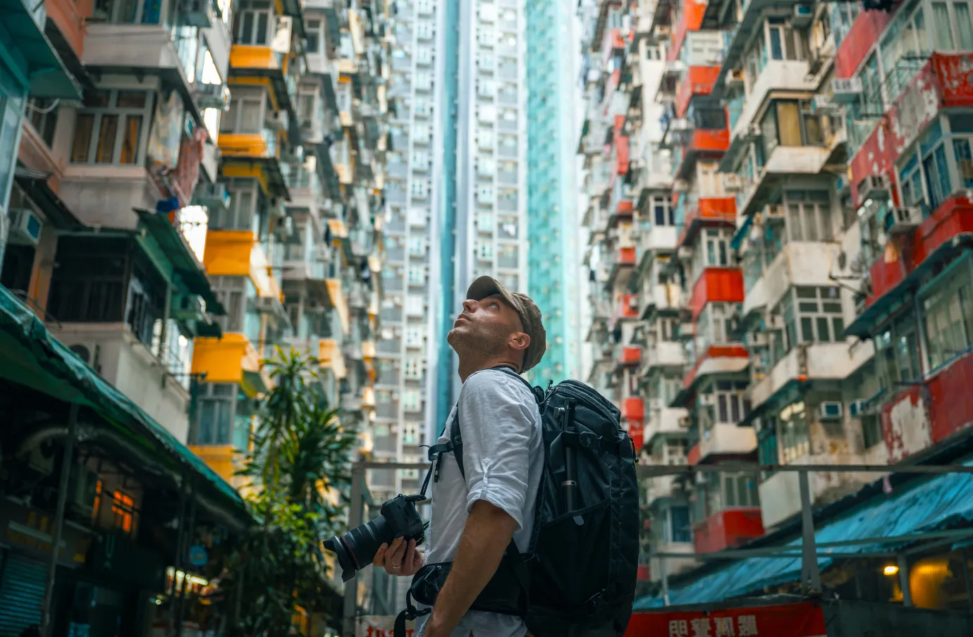 a young man with a backpack and solo travel insurance looks up at buildings in a city street 