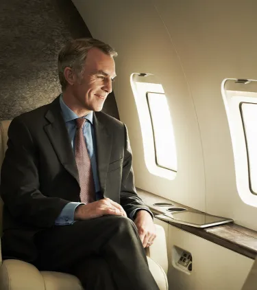an older man with flight insurance sits by an airplane window looking outside during a commercial flight