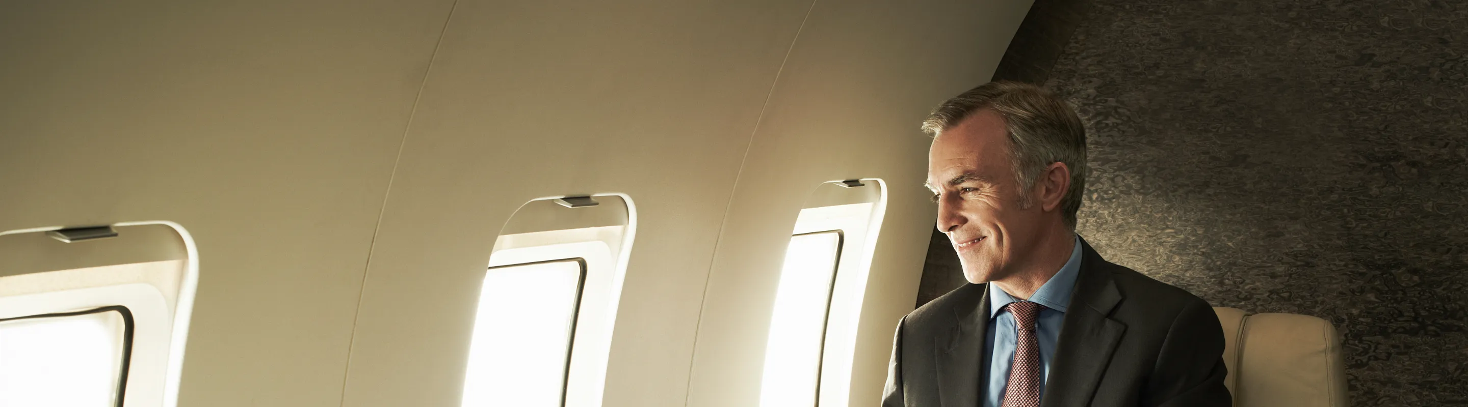 an older man with flight insurance sits by an airplane window looking outside during a commercial flight