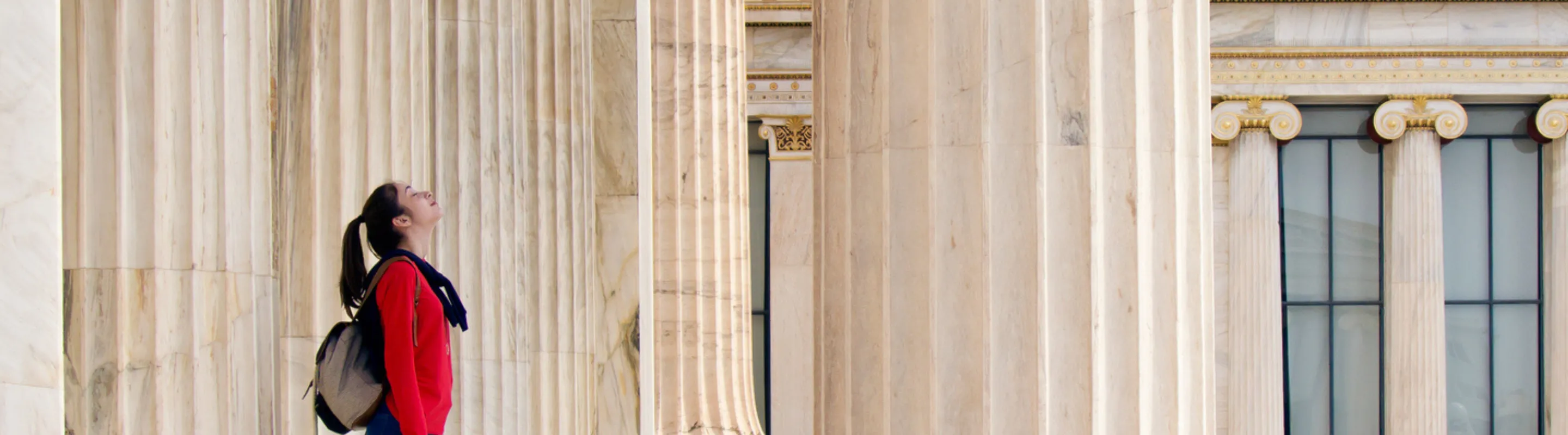 a young woman with cancel for any reason travel insurance awes at classical architecture as she stands between marble columns 