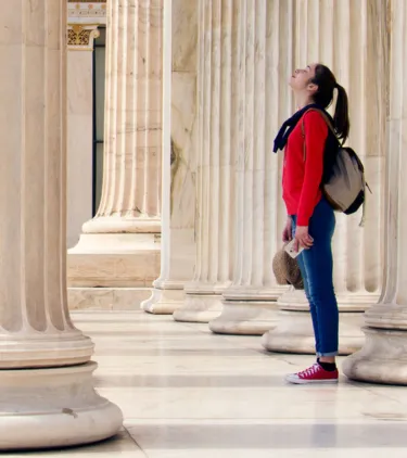 a young woman with cancel for any reason travel insurance awes at classical architecture as she stands between marble columns 