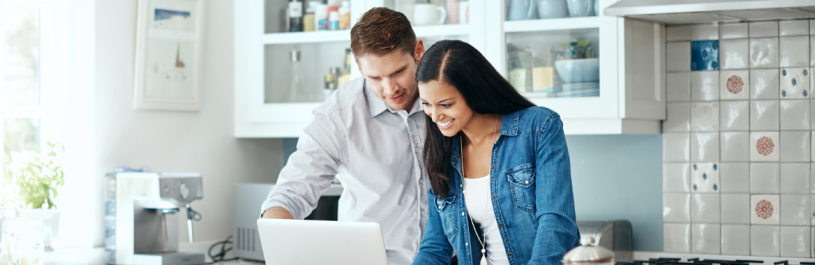 Smiling couple trying to calculate trip cost for their travel insurance policy.