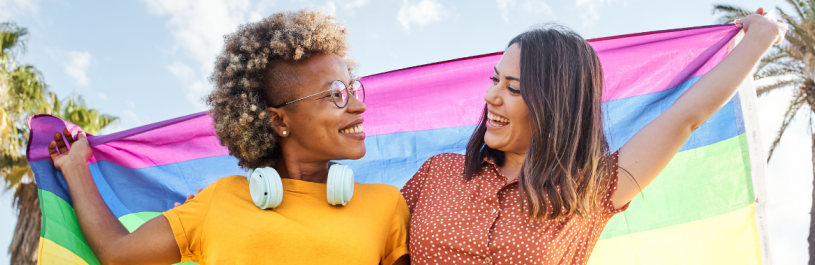 Two smiling women holding a pride flag during their LGTBQ+ travel.
