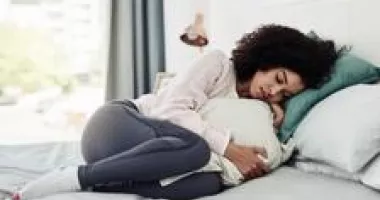 Woman curled up uncomfortably in bed