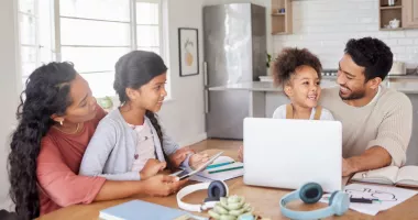 Family of four sitting at the kitchen table with a laptop looking at a travel insurance checklist.