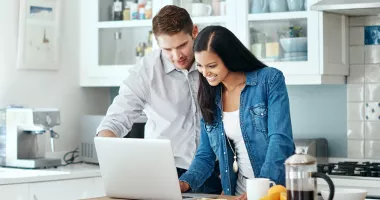 Smiling couple trying to calculate trip cost for their travel insurance policy.