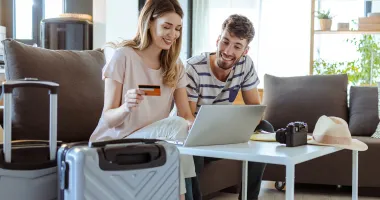 Young couple with laptop and suitcases choosing between credit card travel insurane and a policy.