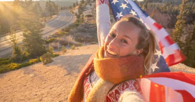 Young woman smiling and taking a selfie while holding an American flag, highlighting the use of a United States travel guide