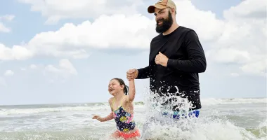 father holding daughter's hand and walking through waves in the Florida ocean during hurricane season