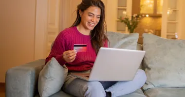 Young woman holding a credit card and using her laptop to look up how much is travel insurance