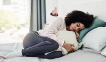 Woman curled up uncomfortably in bed