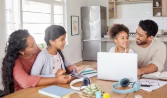 Family of four sitting at the kitchen table with a laptop looking at a travel insurance checklist.