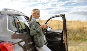 Woman by a car looking at her phone after a vehicle accident on vacation