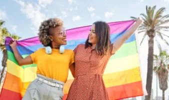 Two smiling women holding a pride flag during their LGTBQ+ travel.