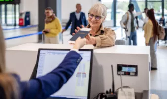 Senior woman smiling and receiving her passport at airport counter may wonder, "Do I need a REAL ID to fly?"