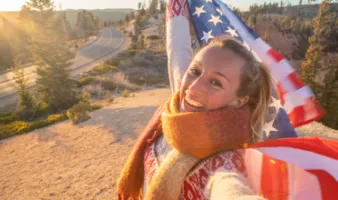 Young woman smiling and taking a selfie while holding an American flag, highlighting the use of a United States travel guide