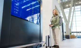 senior woman smiling at the flight monitor in the airport and wondering if travel insurance covers flight disruptions