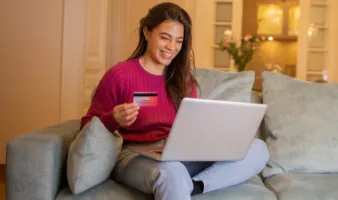 Young woman holding a credit card and using her laptop to look up how much is travel insurance