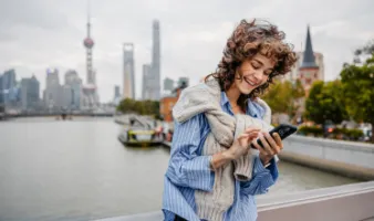 Young woman using our travel app on her smartphone with Shanghai in the background