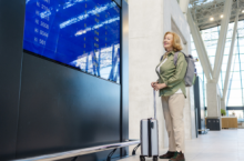 senior woman smiling at the flight monitor in the airport and wondering if travel insurance covers flight disruptions