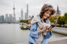 Young woman using our travel app on her smartphone with Shanghai in the background