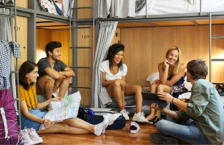 Five young adults laughing and talking in a hostel after researching are hostels safe
