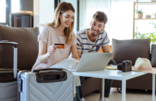 Young couple with laptop and suitcases choosing between credit card travel insurane and a policy.