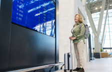 senior woman smiling at the flight monitor in the airport and wondering if travel insurance covers flight disruptions