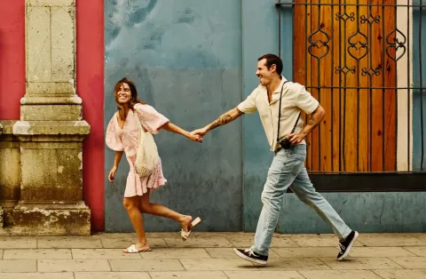 couple holds hands while walking past colorful colonial buildings in Mexico