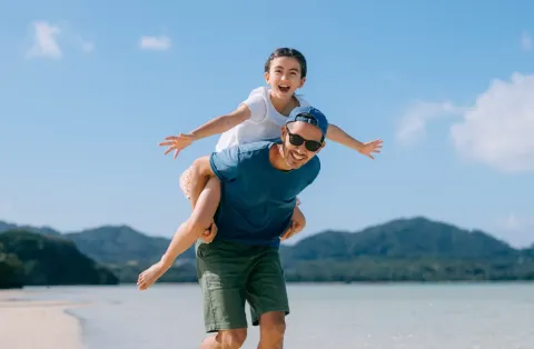 a father gives his daughter a piggyback ride along a sunny tropical beach